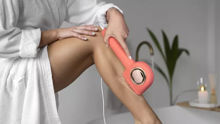 A woman with beautiful legs in white robe doing IPl hair removal at home in a beautiful space